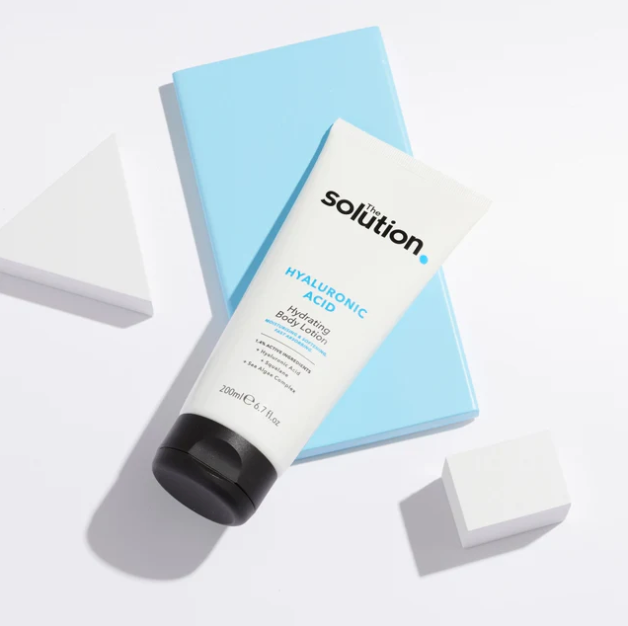 Tube of 'The Solution' Hyaluronic Acid Hydrating Body Lotion on a light blue box with a white background.