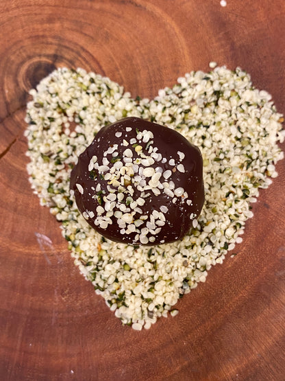 Hemp Farm® Hemp Heart protein ball with hemp heart sprinkles on a heart-shaped arrangement of hemp hearts on a wooden surface.