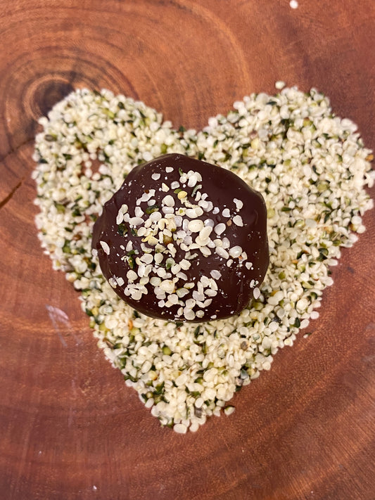 Hemp Farm® Hemp Heart protein ball with hemp heart sprinkles on a heart-shaped arrangement of hemp hearts on a wooden surface.
