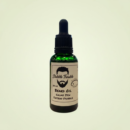 Bottle of 'Stubble Trouble' beard oil on a wooden table with a blurred indoor background