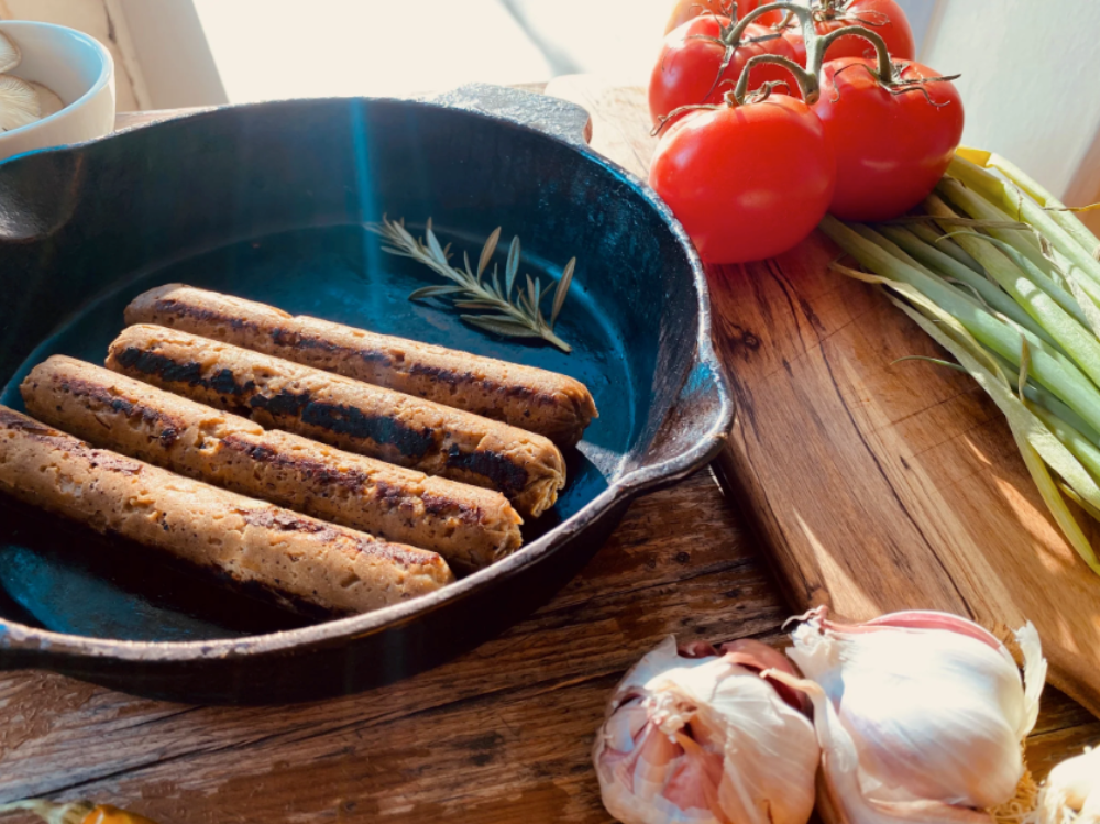 Grilled Let Them Eat Vegan NOT Bratwurst  in a blue skillet on a wooden surface with tomatoes and garlic.