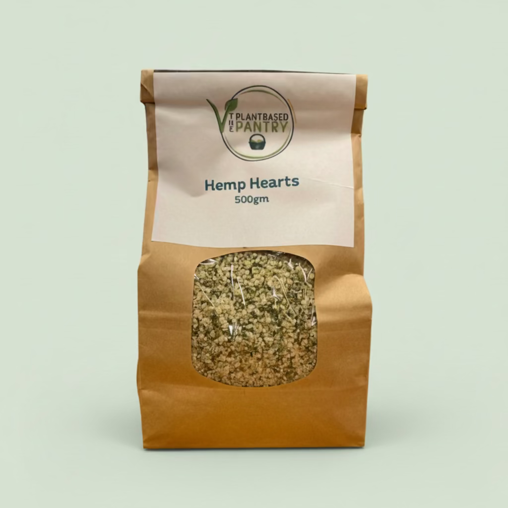 A 500g paper bag of Hemp Hearts from PlantBased Pantry, featuring a clear window showing the textured hemp seeds inside, set on a wooden table.