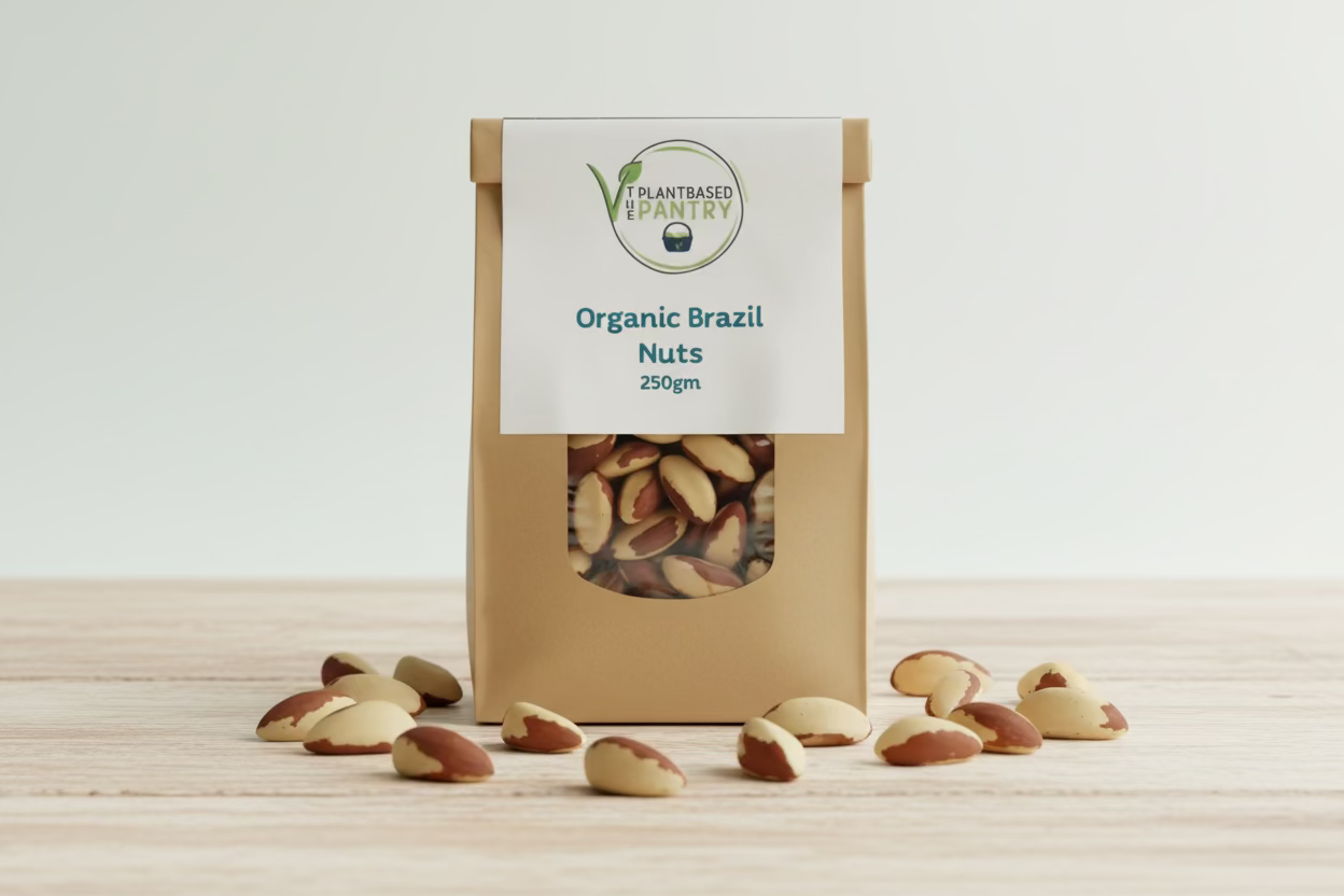 A brown kraft paper bag of 'The Plant Based Pantry' Organic Brazil Nuts, 250g, sitting on a wooden table with a blurred background.