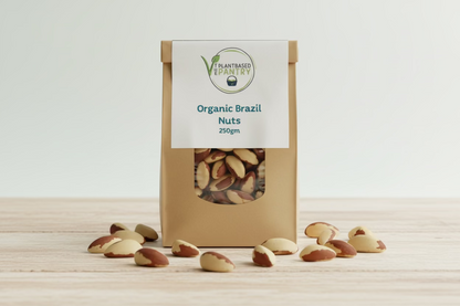 A brown kraft paper bag of 'The Plant Based Pantry' Organic Brazil Nuts, 250g, sitting on a wooden table with a blurred background.