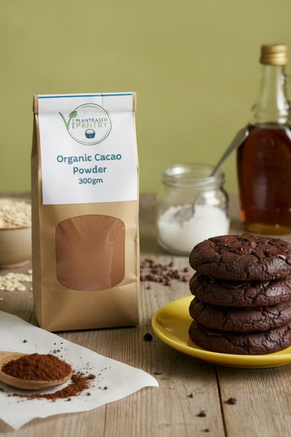 A 300g bag of Plantbased Pantry Organic Cacao Powder on a wooden surface. The packaging consists of a brown kraft paper pouch with a white label at the top and a clear window showing the brown cacao powder inside.