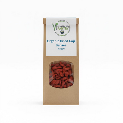 A 100g paper bag of PlantBased Pantry Organic Dried Goji Berries, displayed on a wooden surface. The kraft paper bag features a white label with blue text and a clear window showing the dried red-brown berries inside.