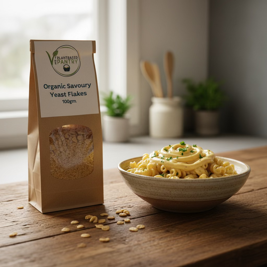 A brown kraft paper bag of Plant Based Pantry Organic Savoury Yeast Flakes, 100g, standing on a wooden counter with a blurred store background.