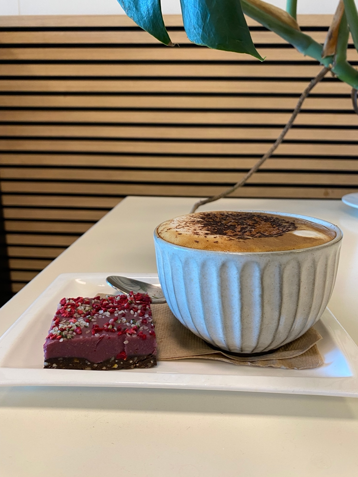 Organic fair trade cappuccino made with gluten free macadamia milk  topped with chocolate, served with a vegan gluen free raspberry and hemp slice